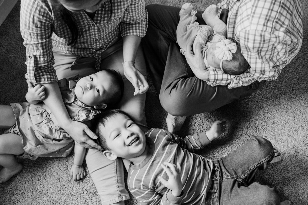 In home lifestyle newborn photograph of family of 5 sitting on the floor snuggling their kids