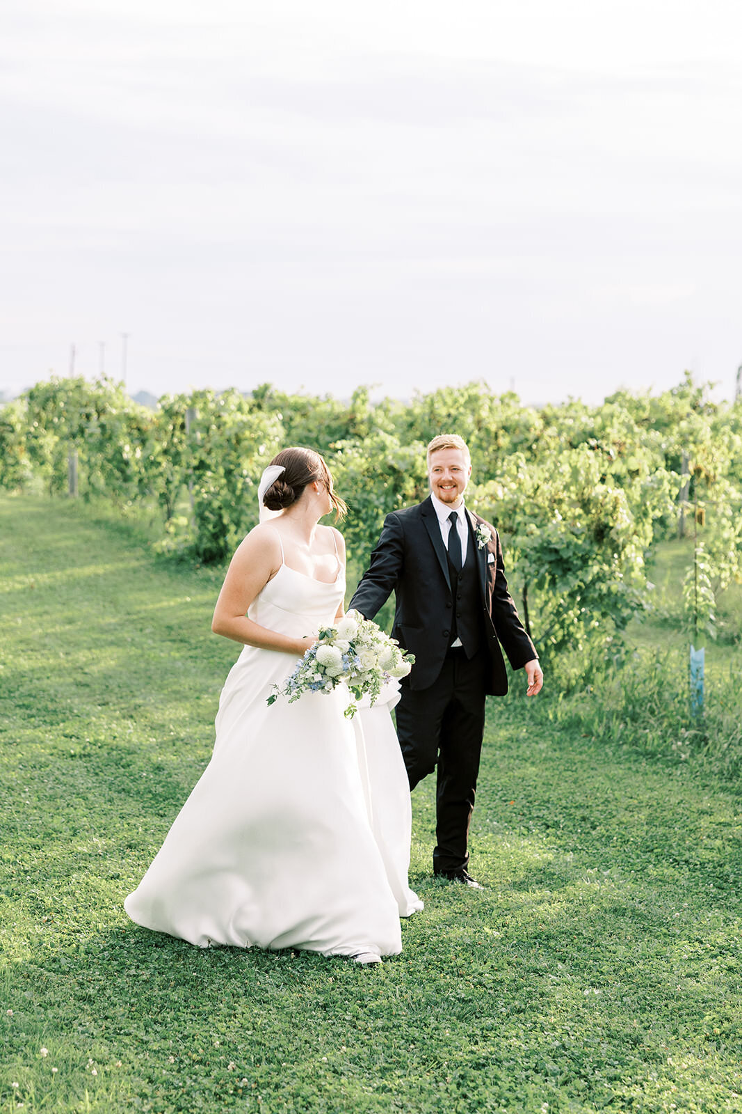 Bride and groom run through a vineyard and smile