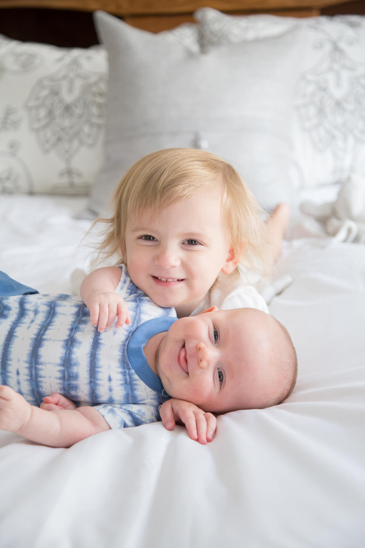 Happy toddler girl and joyful baby brother smiling together on a bed during their session with Las vegas milestone  photographer