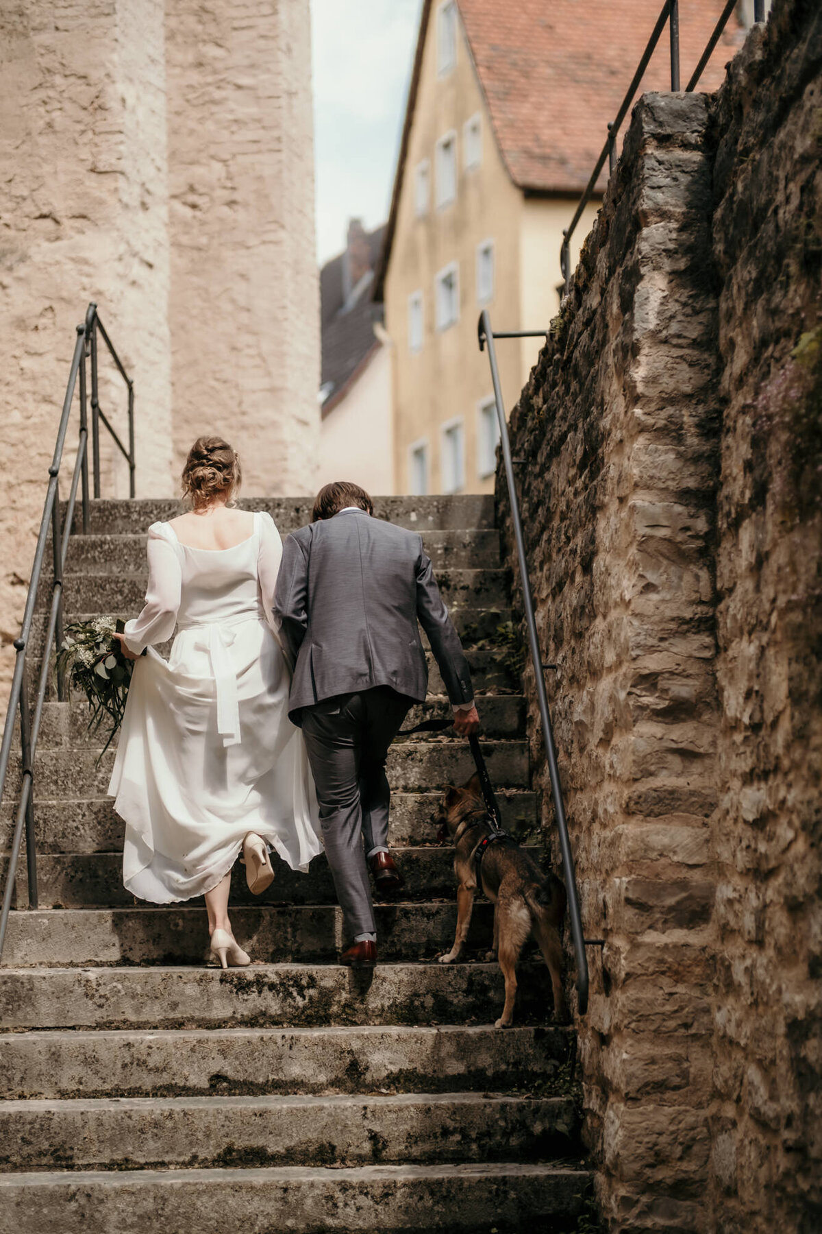 Das Hochzeitspaar läuft zusammen mit ihrem Hund eine Steintreppe hinauf.