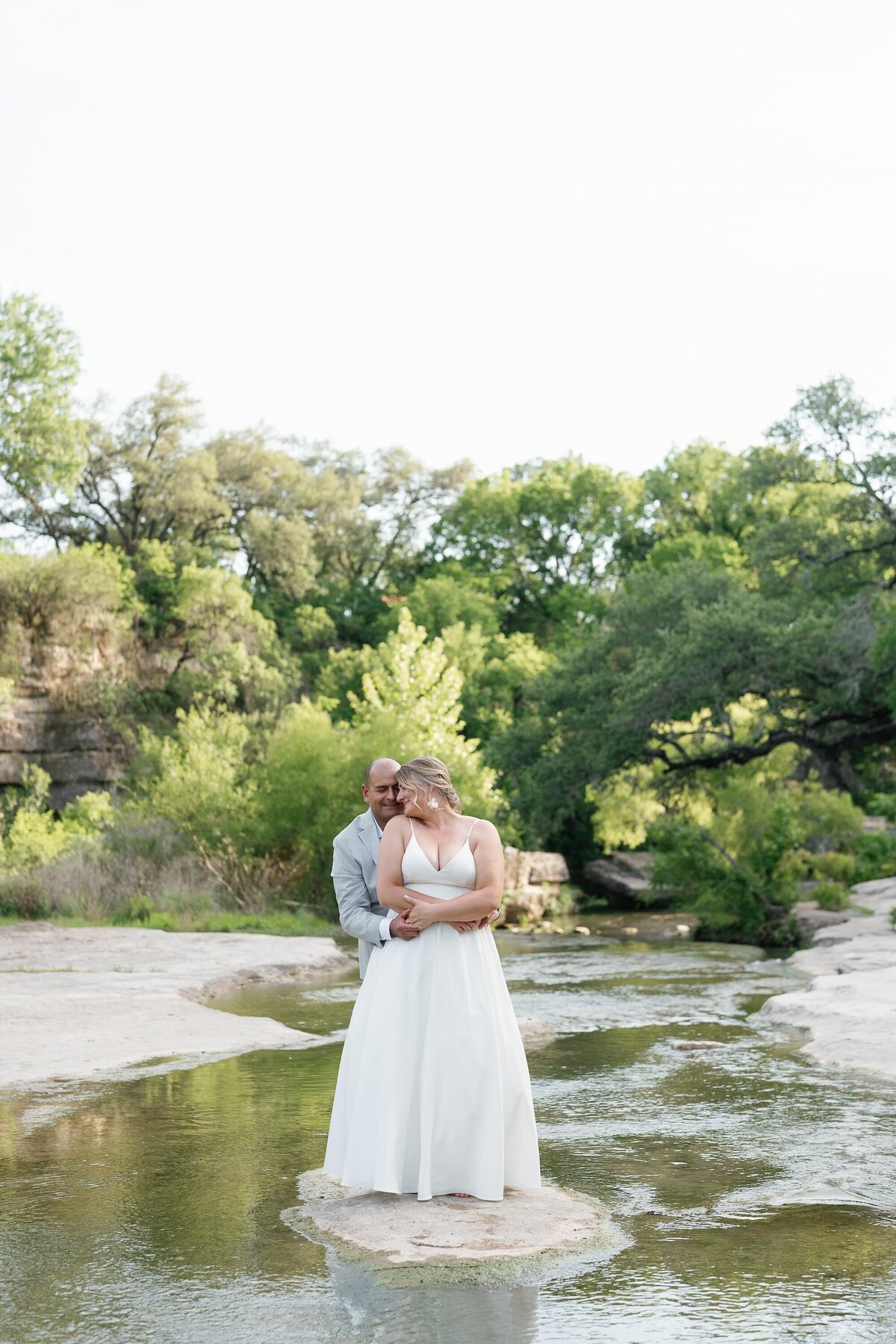 Jen and Miguel embracing on a rock in the middle of an Austin river during their wedding