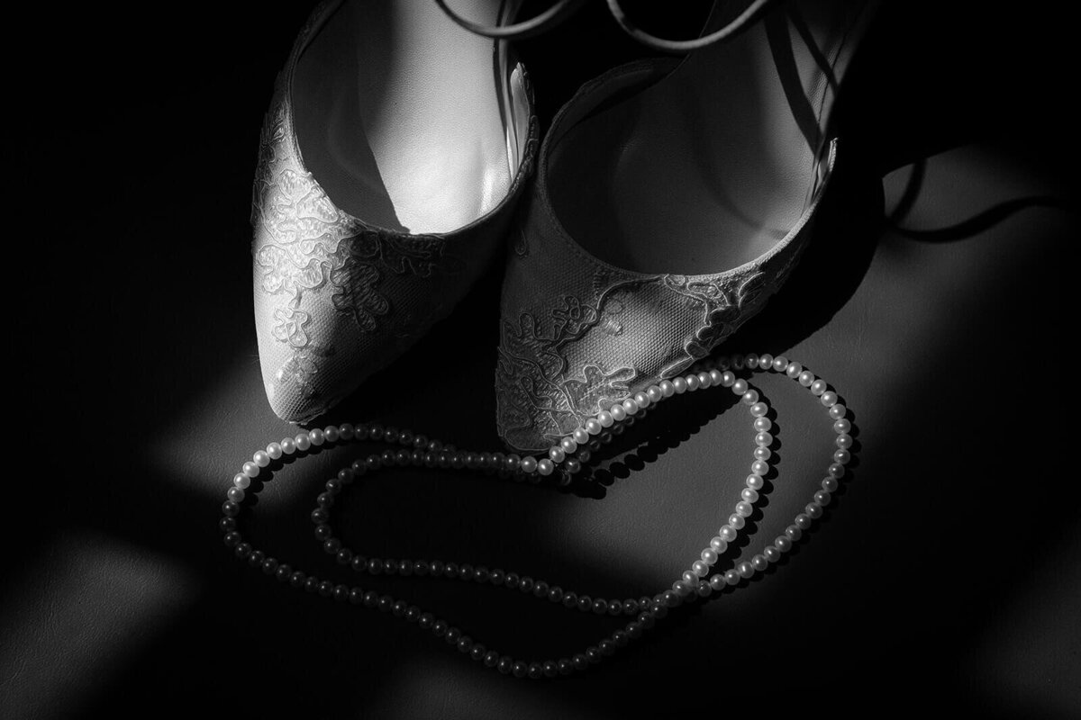 A pair of shoes and a pearl necklace belonging to a bride are lit by a sun light leak