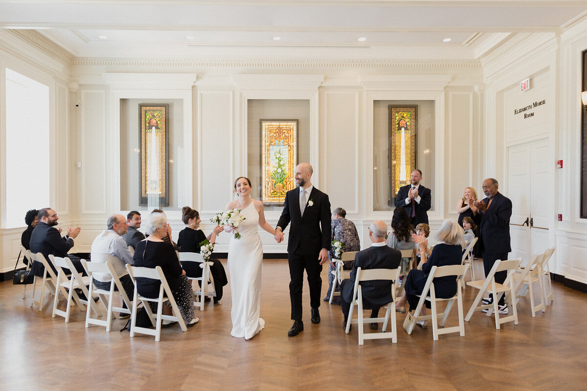 The wedding couple recesses together after the ceremony ends, they're beaming with joy and the gusts applaud.