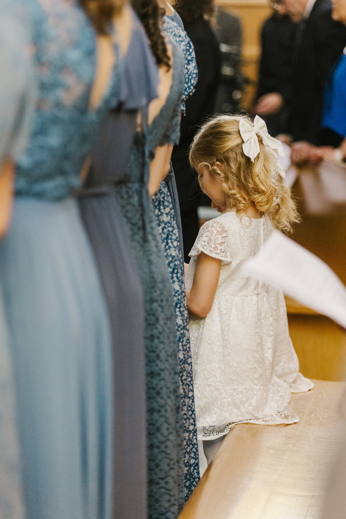 Flower girl in white dress standing in the pews during wedding ceremony