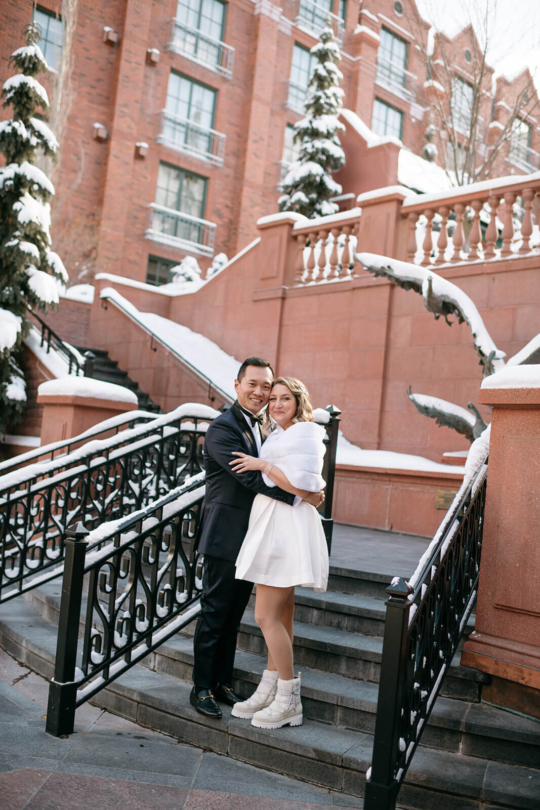 Bride and groom walking down the courtyard stairs at St. Regis Aspen, framed by elegant architecture and a snowy outdoor setting.