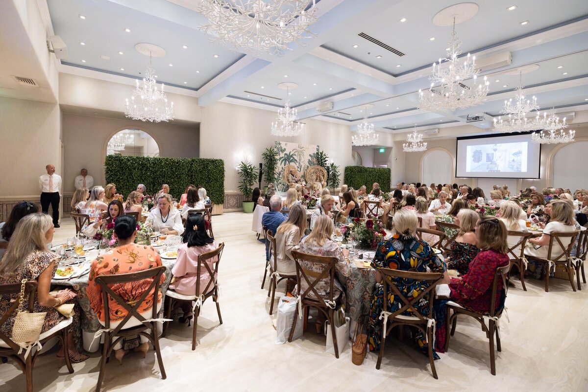 Guests seated in a bright ballroom with chandeliers.