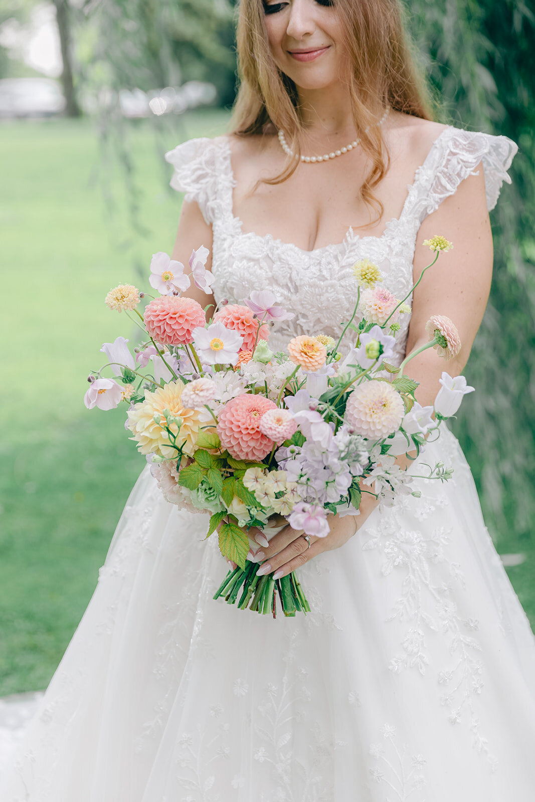 A bride at the Forest and Stream Club holds a large pastel bouquet of spring flowers. 