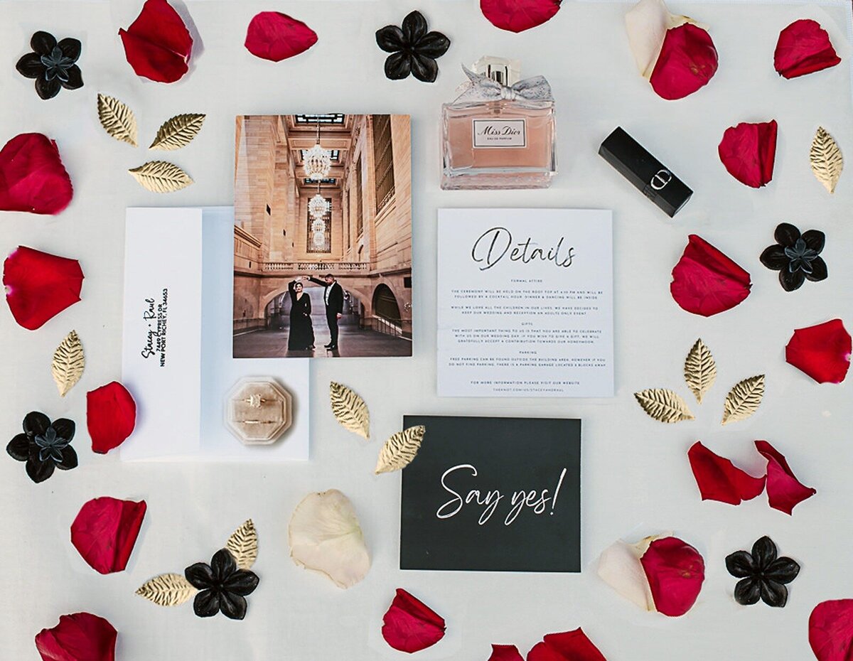 Red, black and gold invitation suite flatlay with things all around.