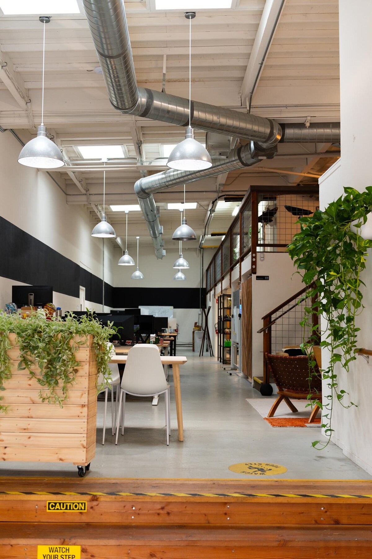 View of an open-concept office with natural wood planters, hanging industrial lights, and workstations along the back wall.