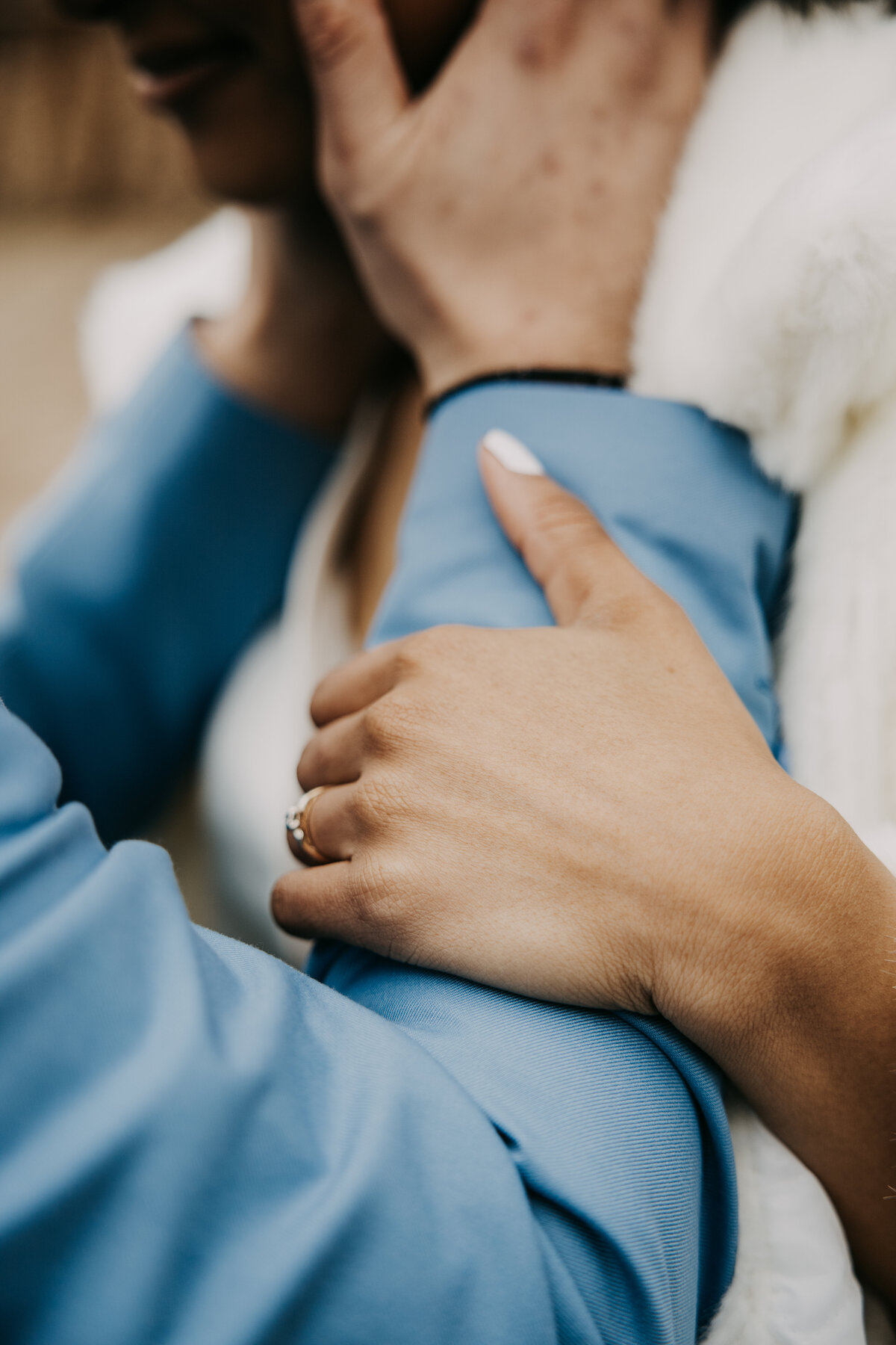 Close-up of a bride holding her groom's forearm, while he holds her face, with focus on her engagement ring.