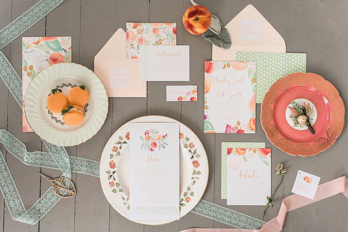 Mismatched vintage wedding china with peach macarons and the groom's peach and blush protea boutonniere. Peach and pink flower stationery suite with peaches, pink flowers, green leaves and a green polka dotted envelope.