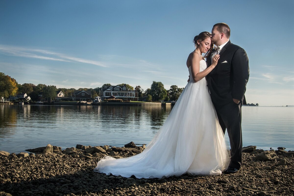 a bride leans her head against the chest of her groom, who kisses her on the forehead