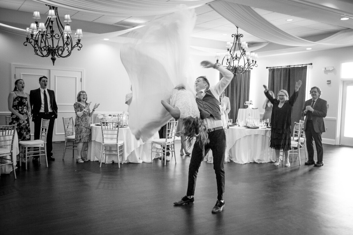 Black and white image of a groom is flipping his bride during their first dance at NorthStone Country Club by Charlotte wedding photographer DeLong Photography