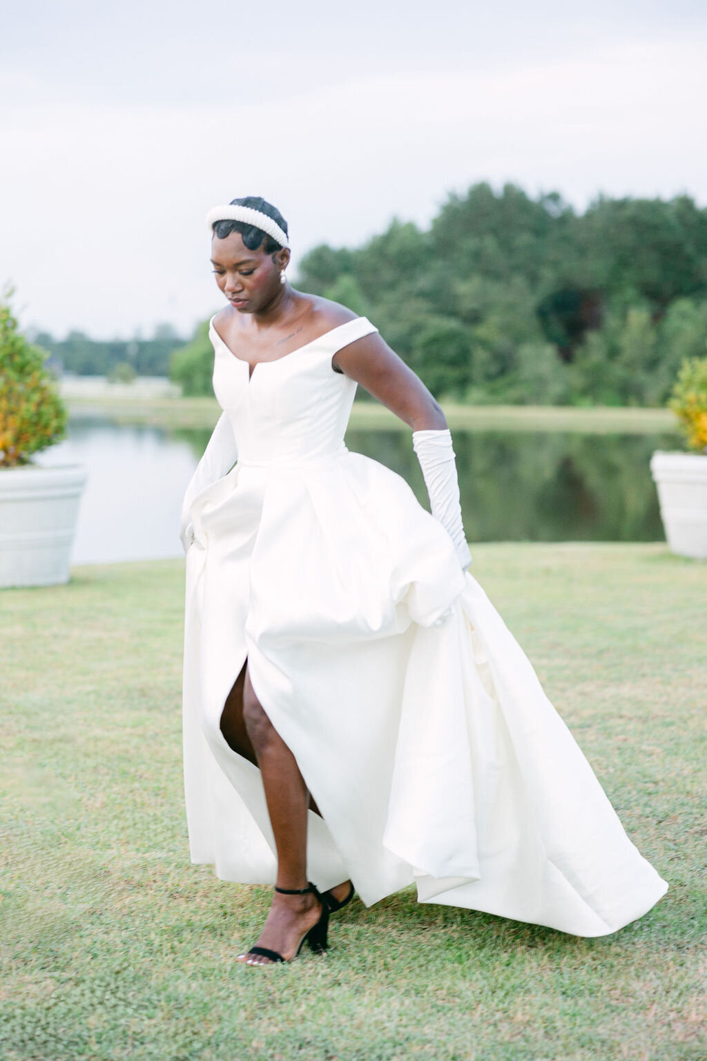 A stylish bride in a modern off-the-shoulder gown walks gracefully across a lush outdoor venue in Savannah, GA, exuding timeless sophistication. Amia Marcell charleston wedding photographer