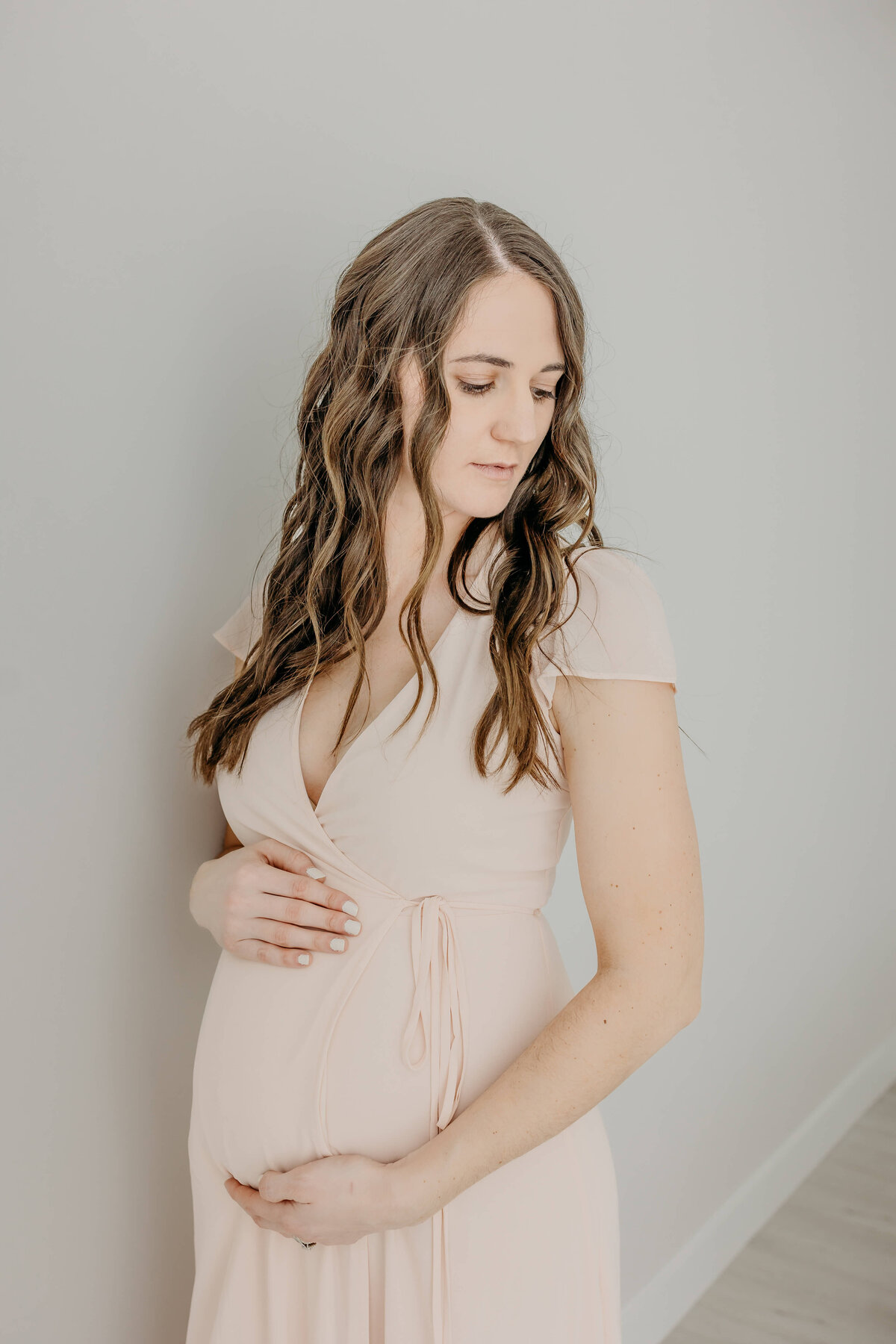 Brunette woman holding pregnant stomach in pink dress