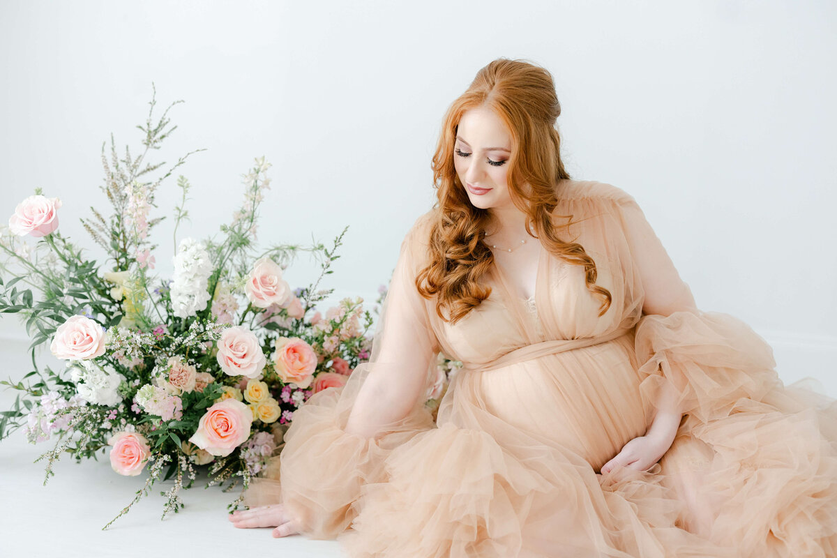 a pregnant woman in a dress sitting next to flowers