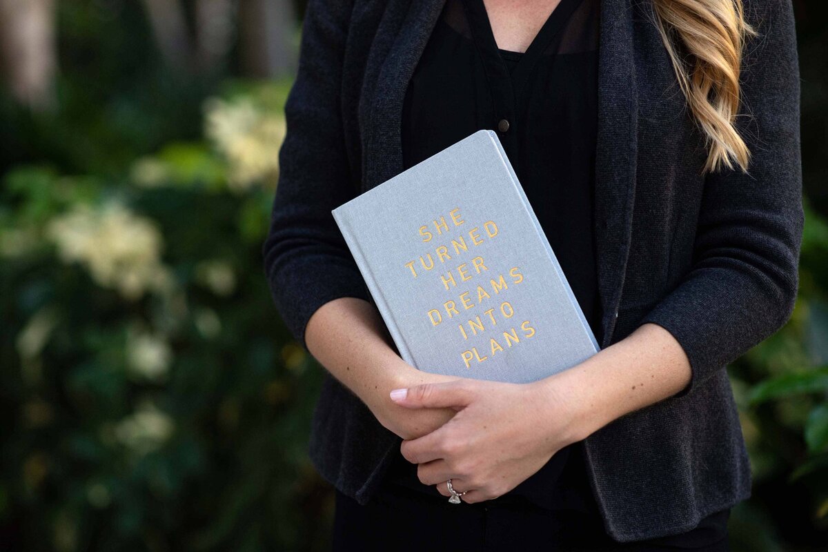 A photo of a women holding a book titled "She Turned Her Dreams into Plans."