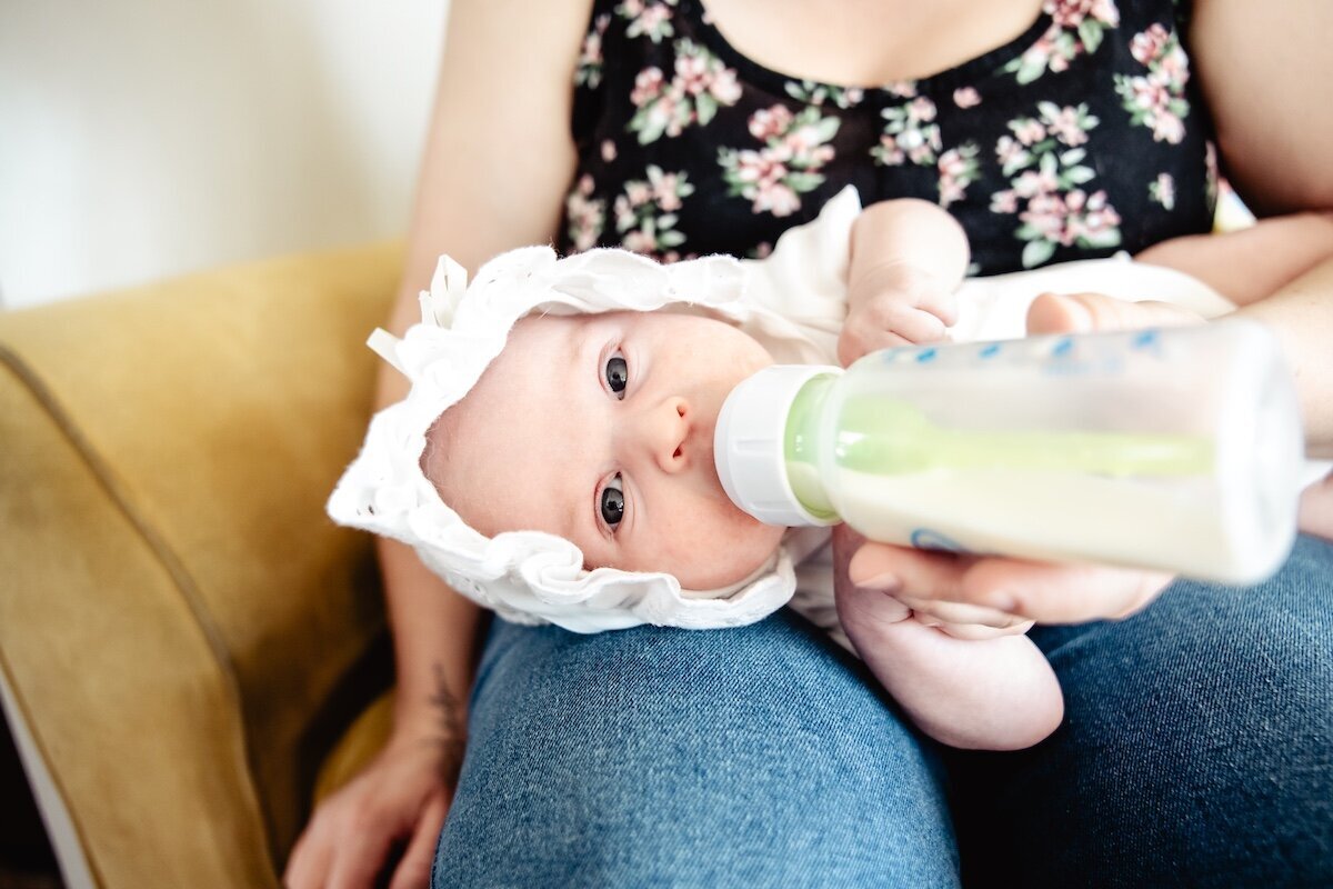 a baby girl wearing a bonnet drinking from a bottle
