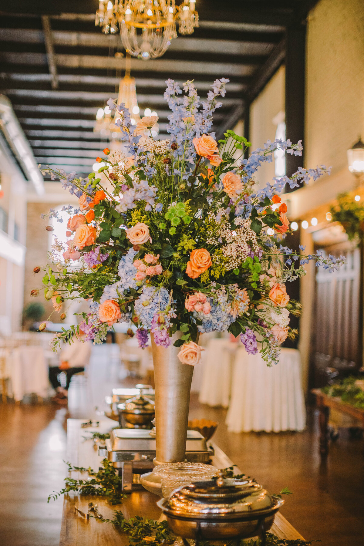 Wedding floral arrangement with peach, blue, and purple flowers.