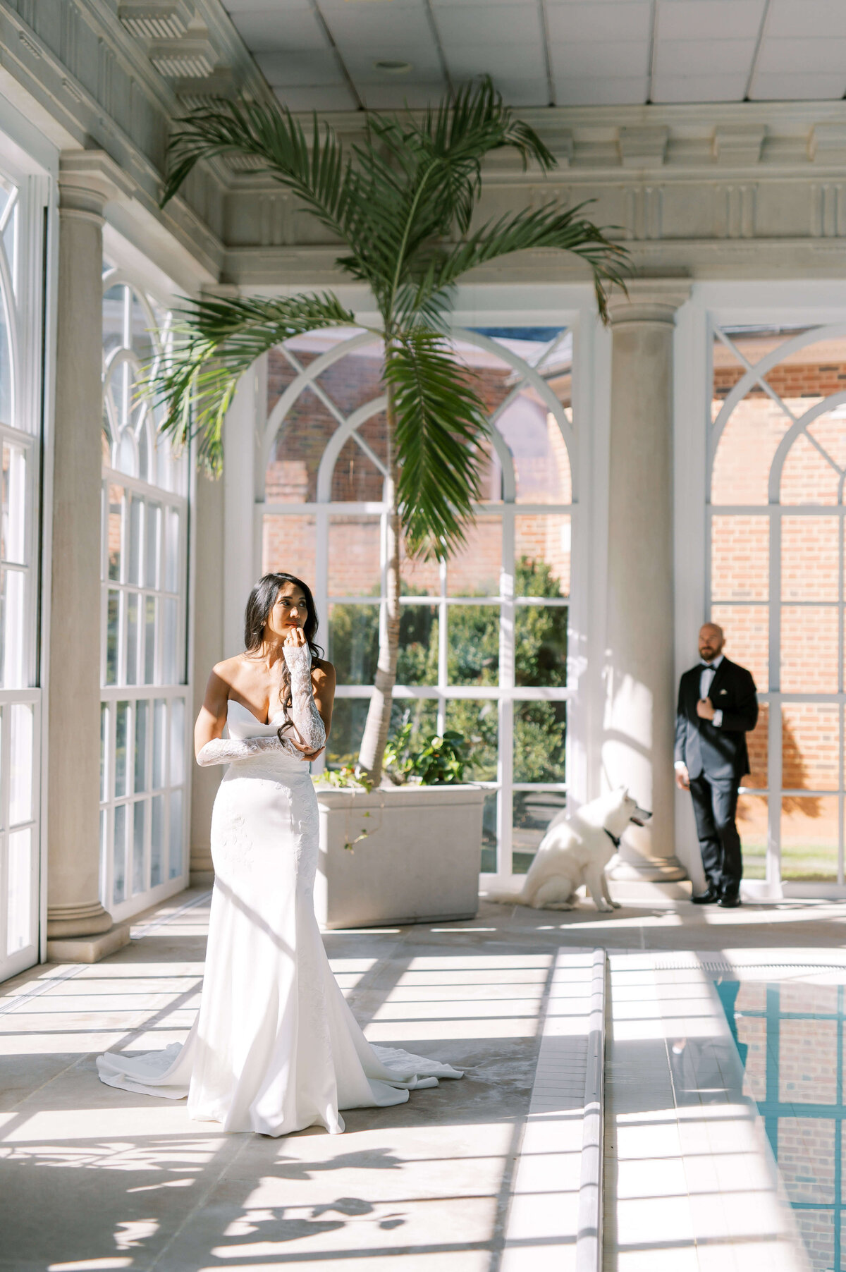 Bride posing for a portrait as groom admires from background before their wedding day at Larz Anderson House