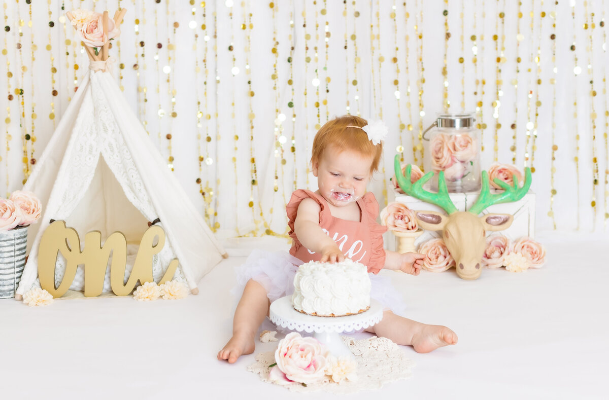 Cake Smash Photographer, a happy baby girl puts her hands in cake at her first birthday