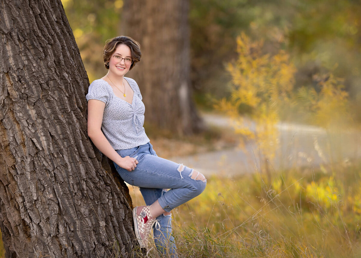 high school senior girl leaning against a tree in a park