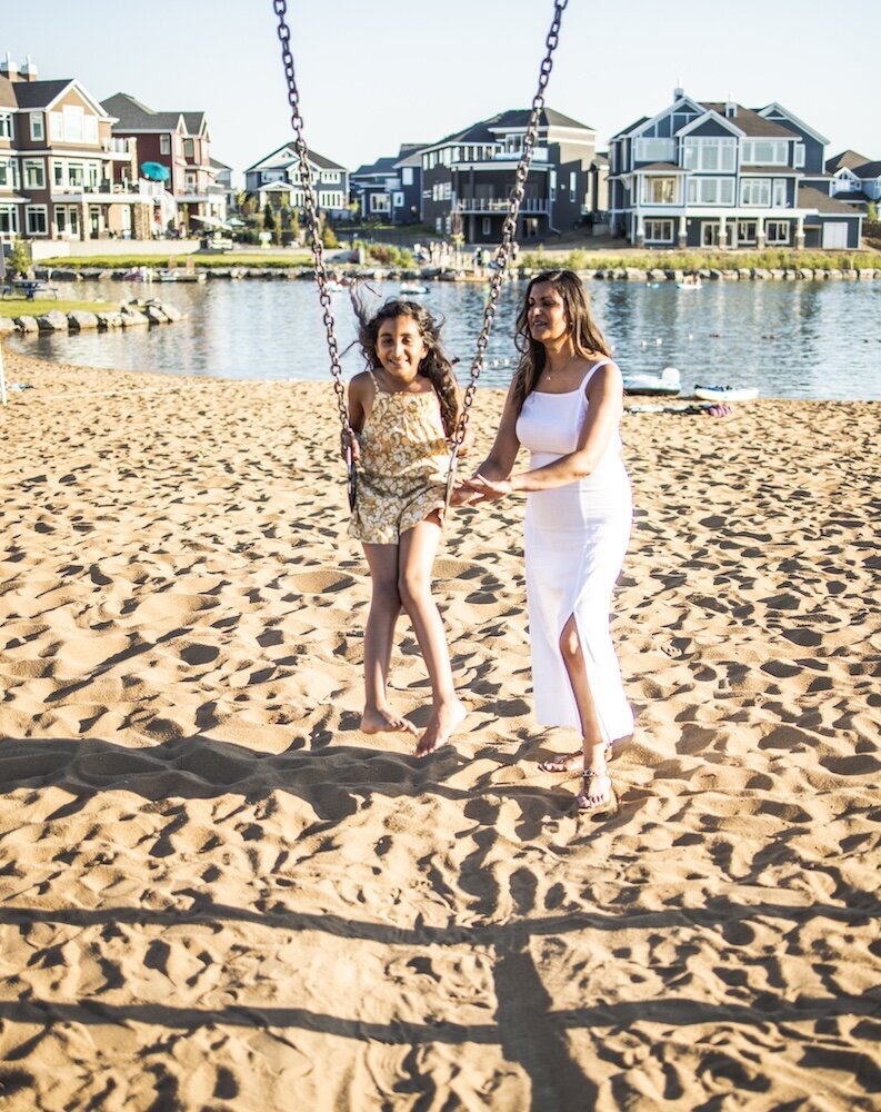 Mom in a white dress pushing her  daughter on a swing 