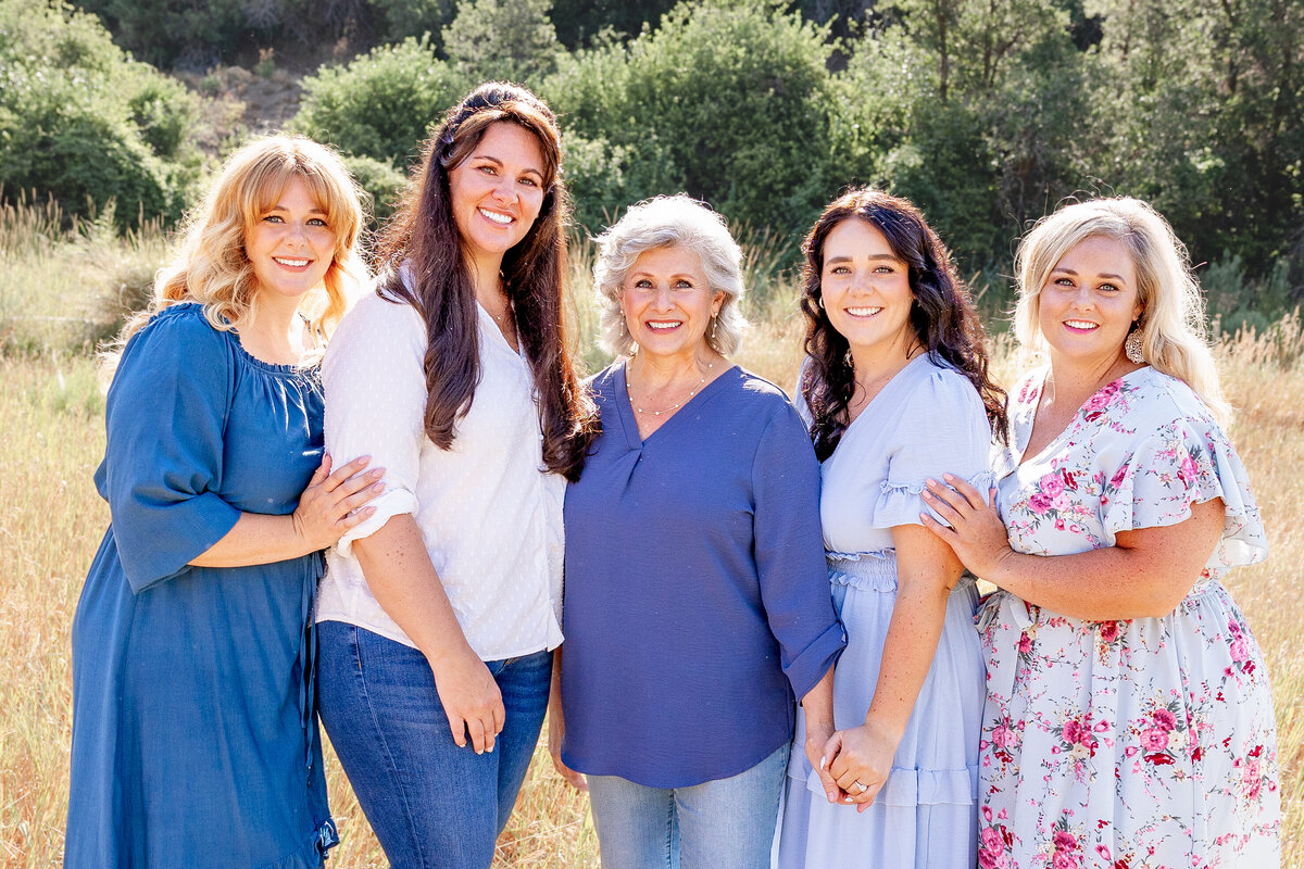 A group of women from different generations, standing together with their arms around each other, dressed in coordinating outfits.