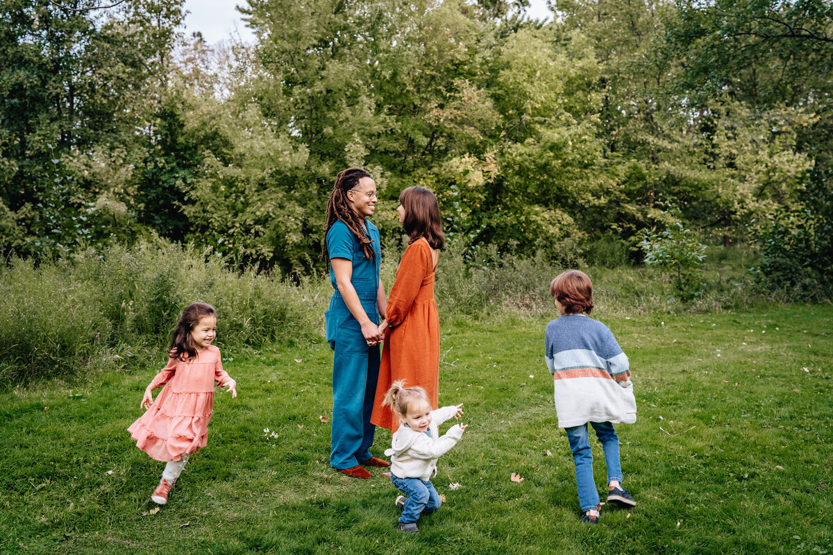 Two parents look at one another and hold hands while their kids run around them.