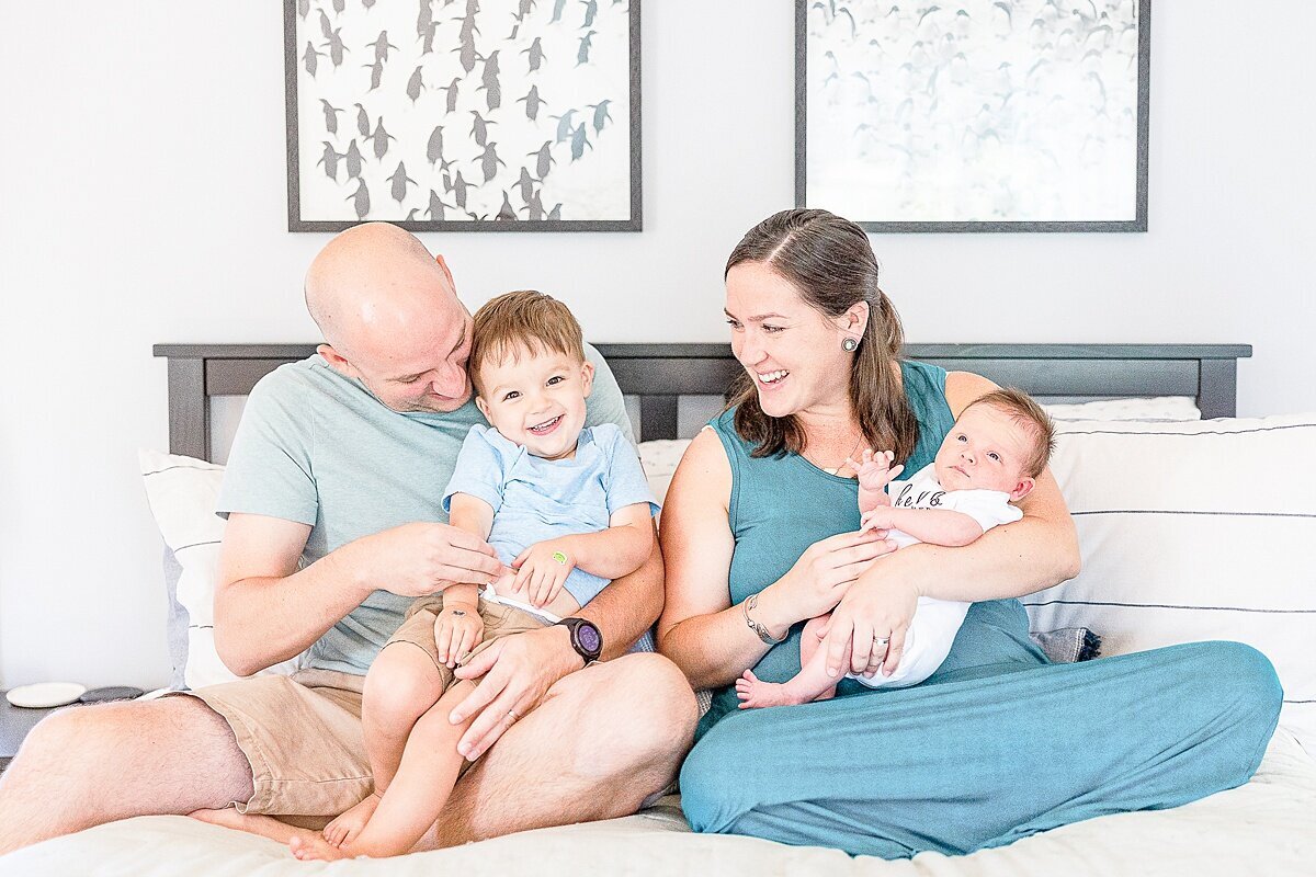 family laoughts together on bed dung in-home newborn photo session with Sara Sniderman Photography in metro west Boston  Massachusetts