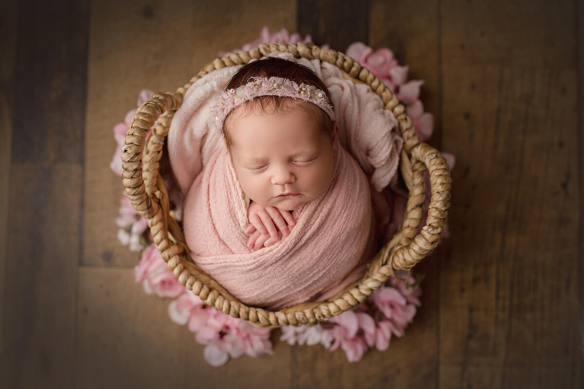 newborn baby wrapped in pink, placed in basket surrounded by pink flowers