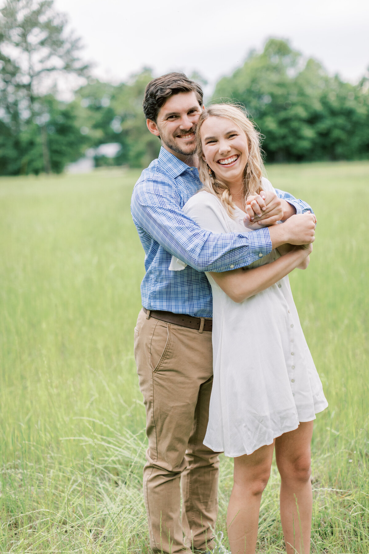 A couple stands in a grassy field for their engagement photos.