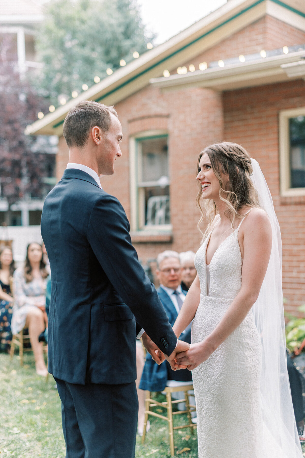 Bride smiling at her groom during outdoor wedding ceremony captured by Pam Kriangkum Photography, fine art, classic wedding photographer in Edmonton, Alberta. Featured on the Bronte Bride Vendor Guide.