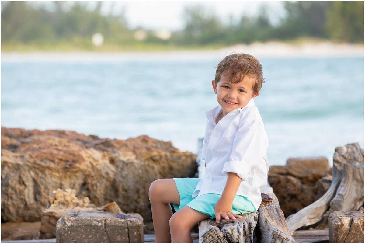 Little boy in blue shorts sitting on rocks at the beach