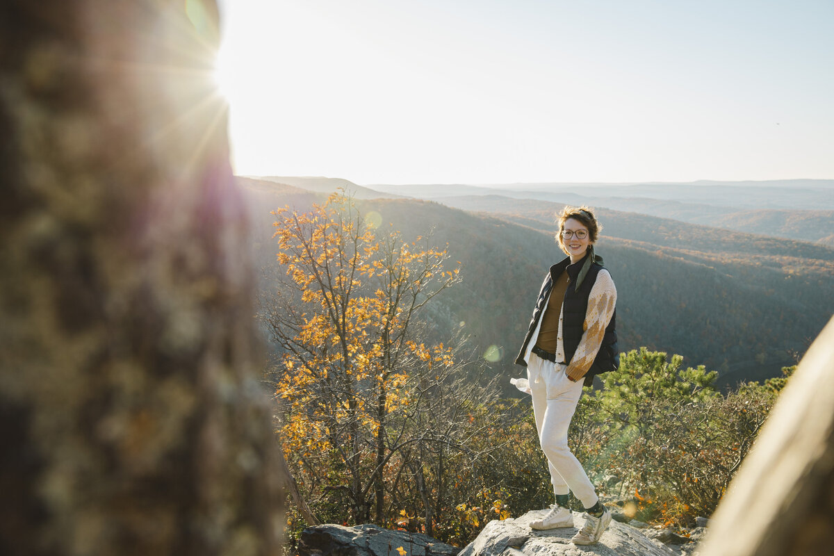 A person standing on a rock overlooking the mountains smiling
