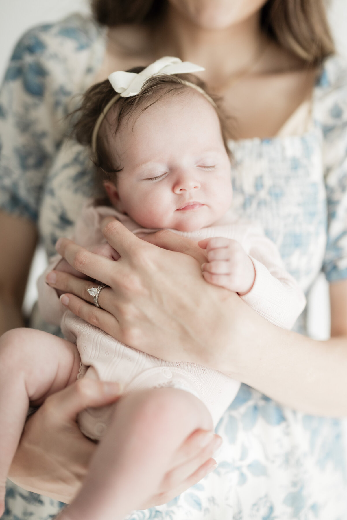 Close-up of a mother’s hands holding a swaddled newborn baby, both wearing floral and soft pastel tones.