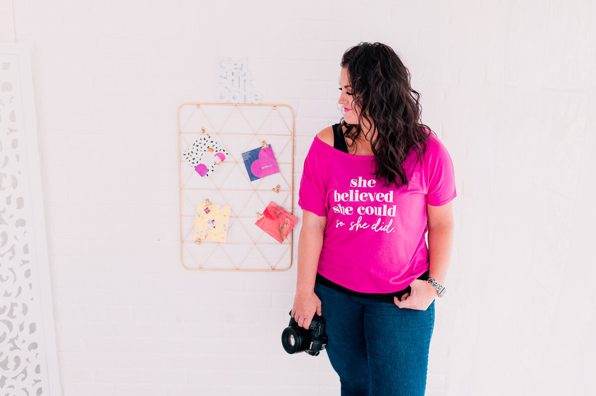Jessi Cabanin standing in front of a white wall with a hot pink she believed she could so she did tshirt.