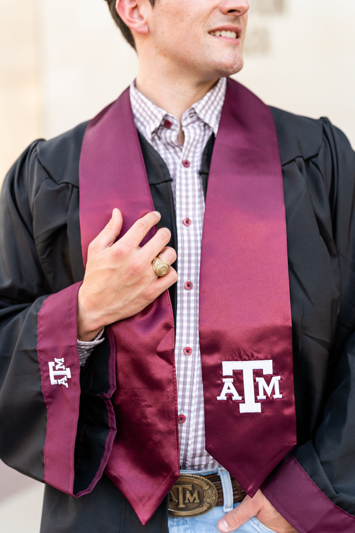 Texas A&M senior guy holding A&M stole while wearing gown and Aggie Ring while smiling away