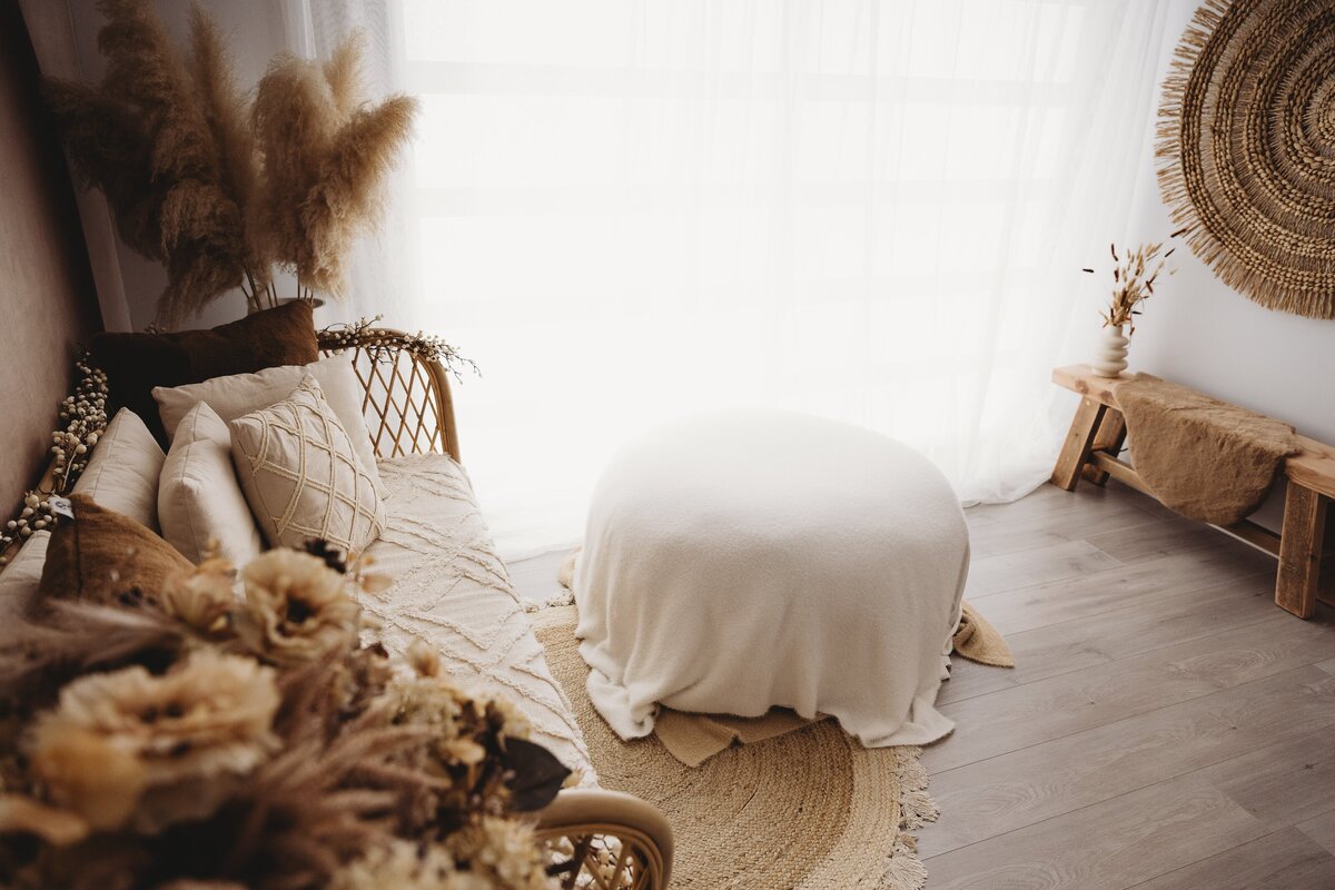 A light-filled room with wicker furniture, a cushioned bench, a large pouf covered with a white blanket, and decorative pampas grass creates the perfect setting for South Coast newborn or Wollongong motherhood sessions. Natural materials and neutral tones dominate the decor.