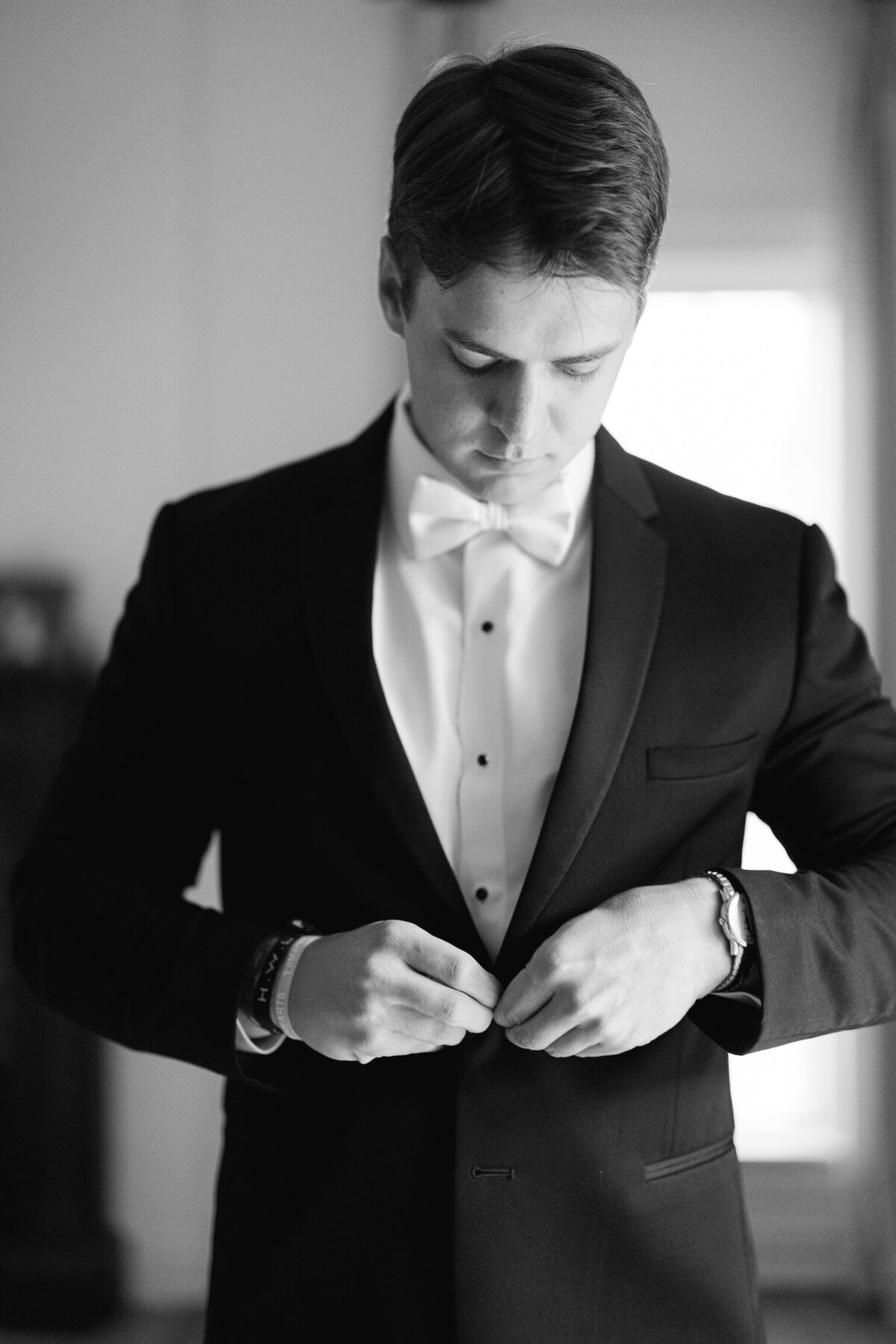 A refined moment as the groom buttons his jacket, preparing for the day with elegance and style, timelessly captured on film by Morgan Alysse, Louisiana film photographer.