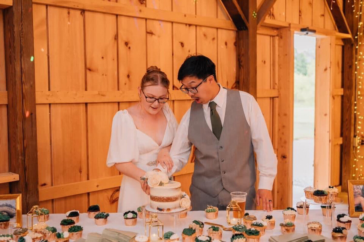 Bride and groom cutting their wedding cake together in a wooden barn