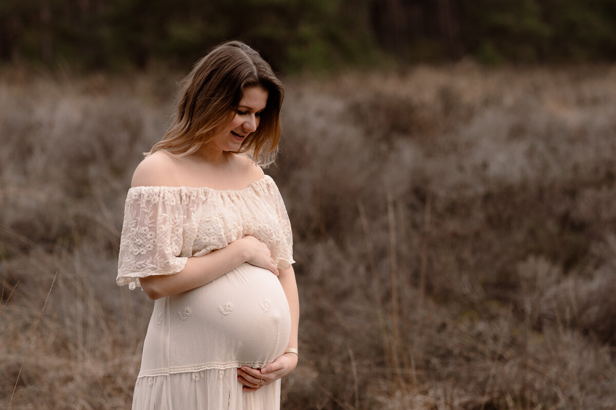 Zwangere vrouw staat in de natuur en kijkt naar haar mooie buik