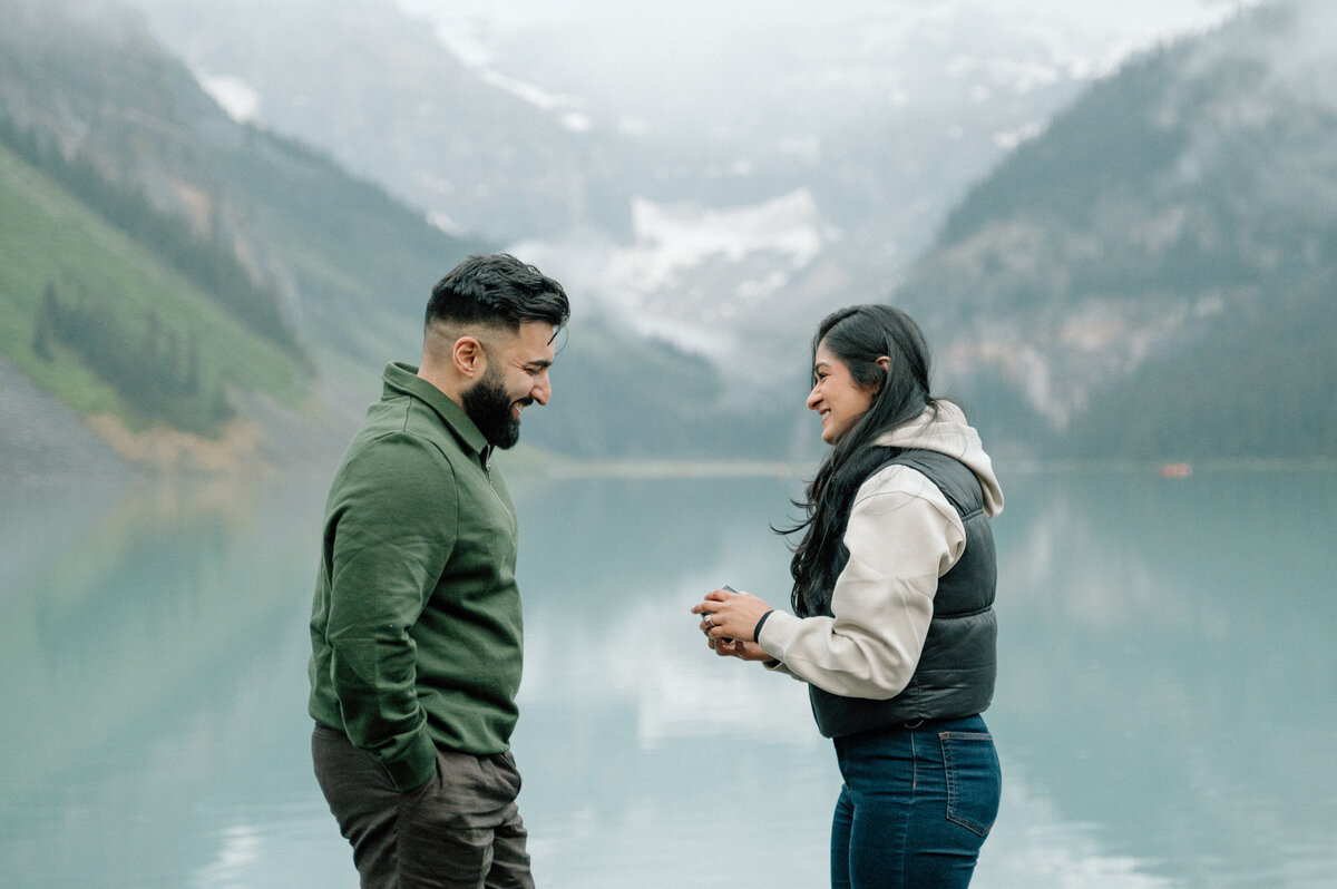 Emotional moment after proposal at Lake Louise with couple holding hands by the lake.