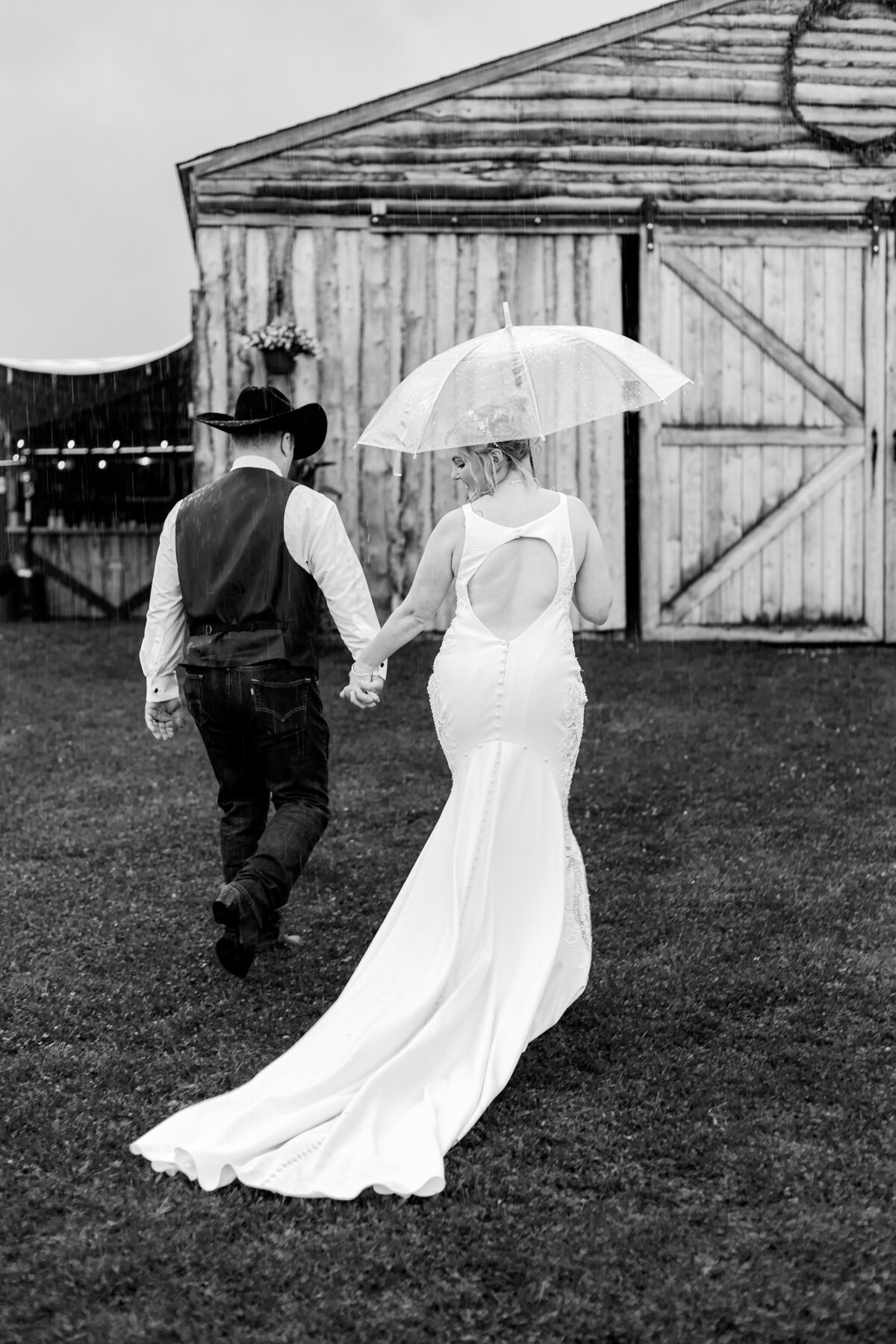 Bride and groom walk towards a barn with an umbrella in hand