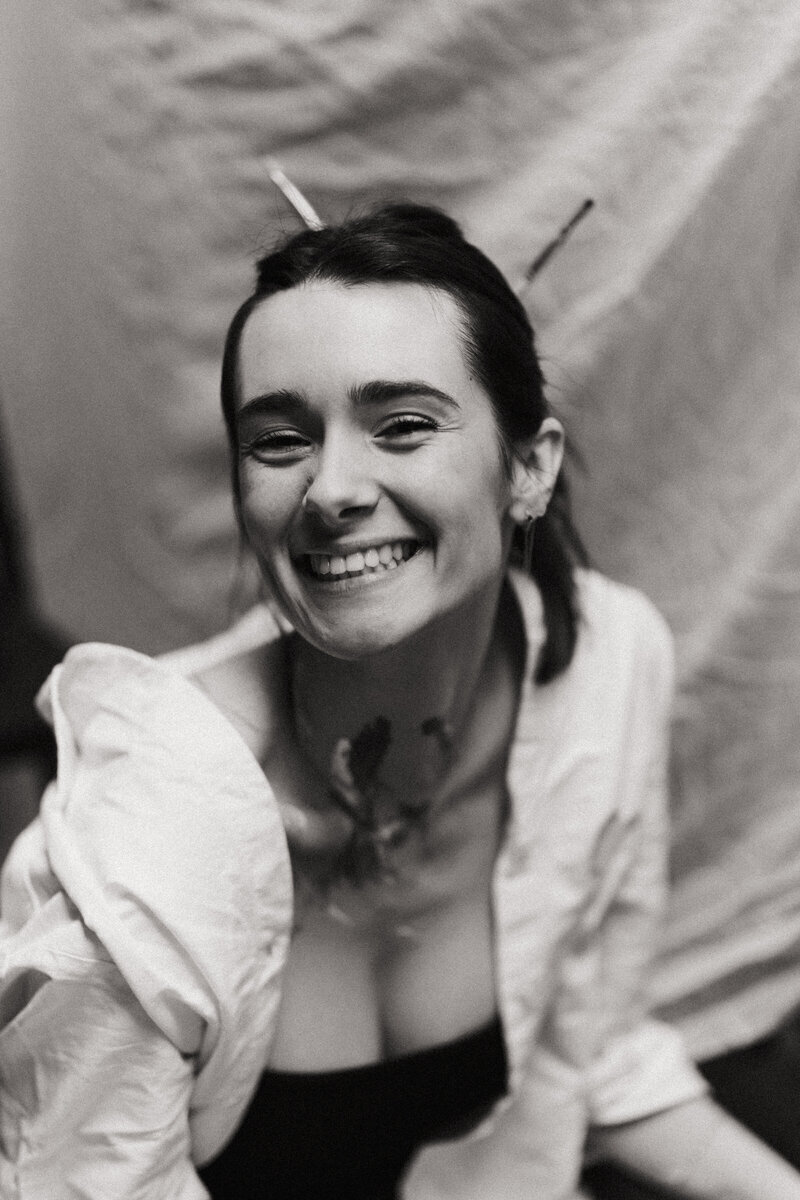 Portrait d'une femme souriante en noir et blanc portant une chemise blanche lors d'une séance photo.