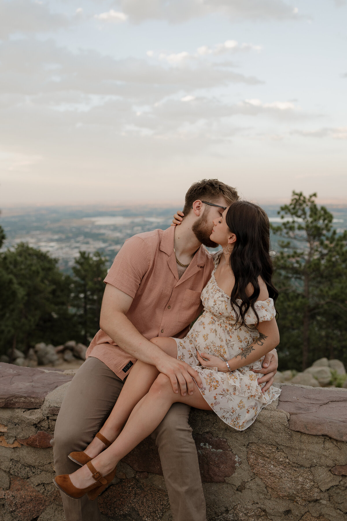 Expectant parents hugging each other while sitting on rock wall