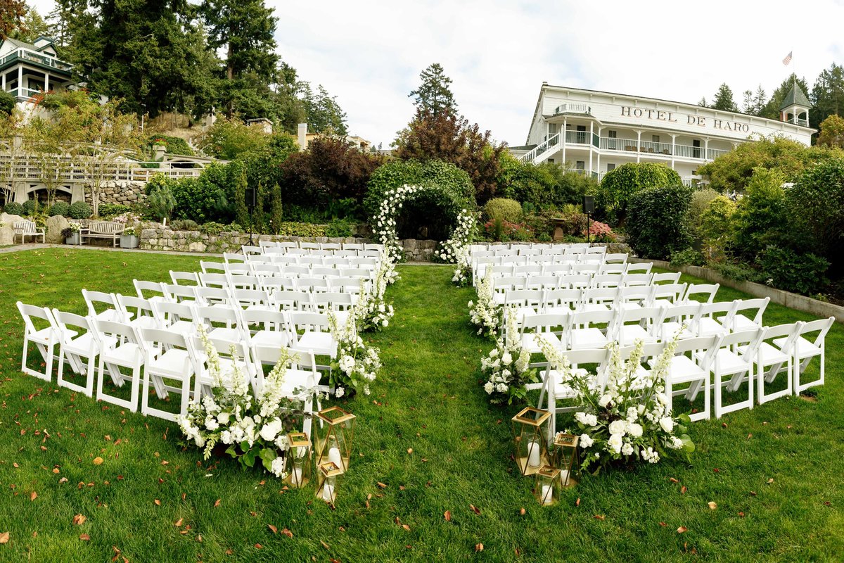 garden wedding ceremony at Roche Harbor Resort with white folding chairs, white aisle flowers and a circle arch with white roses