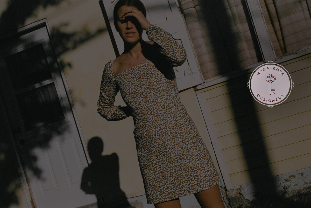 Female wearing floral print dress outside in front of yellow house with heavy shadow