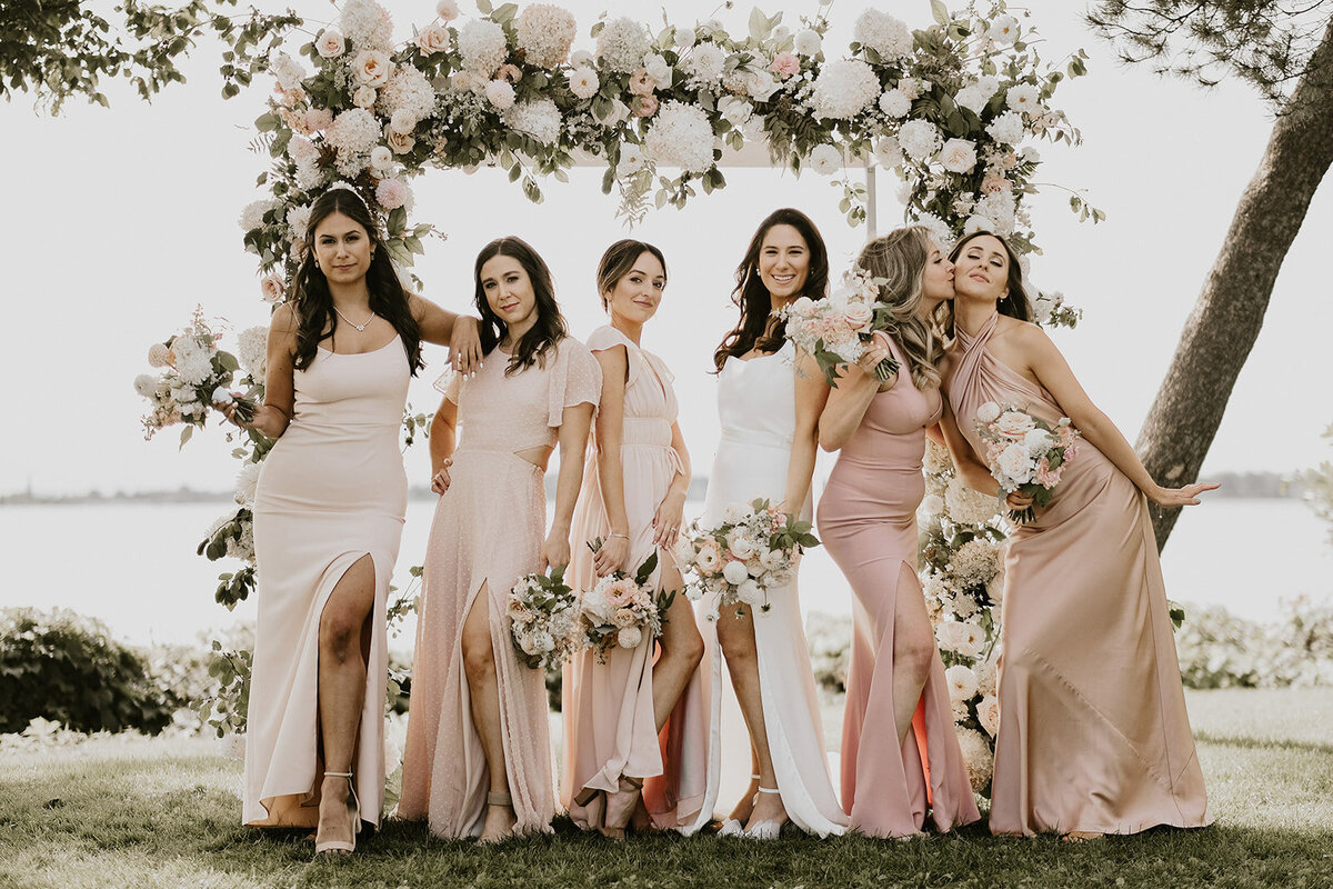 A bridal party poses by an arch of white flowers at the Forest and Stream Club .