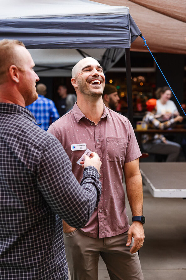 Man in pink shirt throws his head back and laughs while talking to a friend.